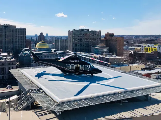Black helicopter parked on a rooftop helipad overlooking a city skyline on a sunny day