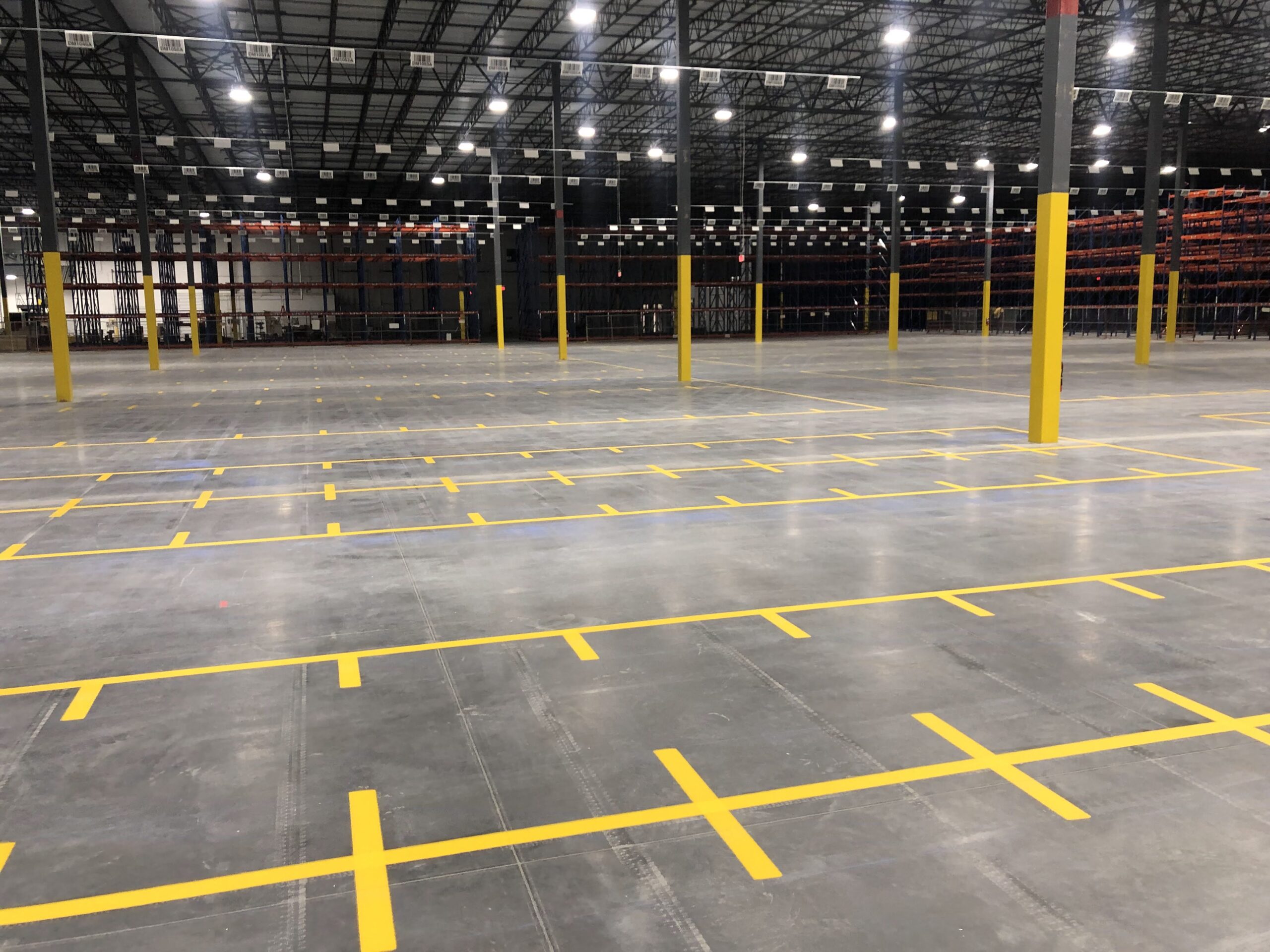 Empty warehouse interior with yellow safety posts and marked floor lanes under bright overhead lights.