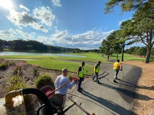 Maintenance crew in highvisibility vests working along a paved lakeside path handling hoses and equipment on a sunny day