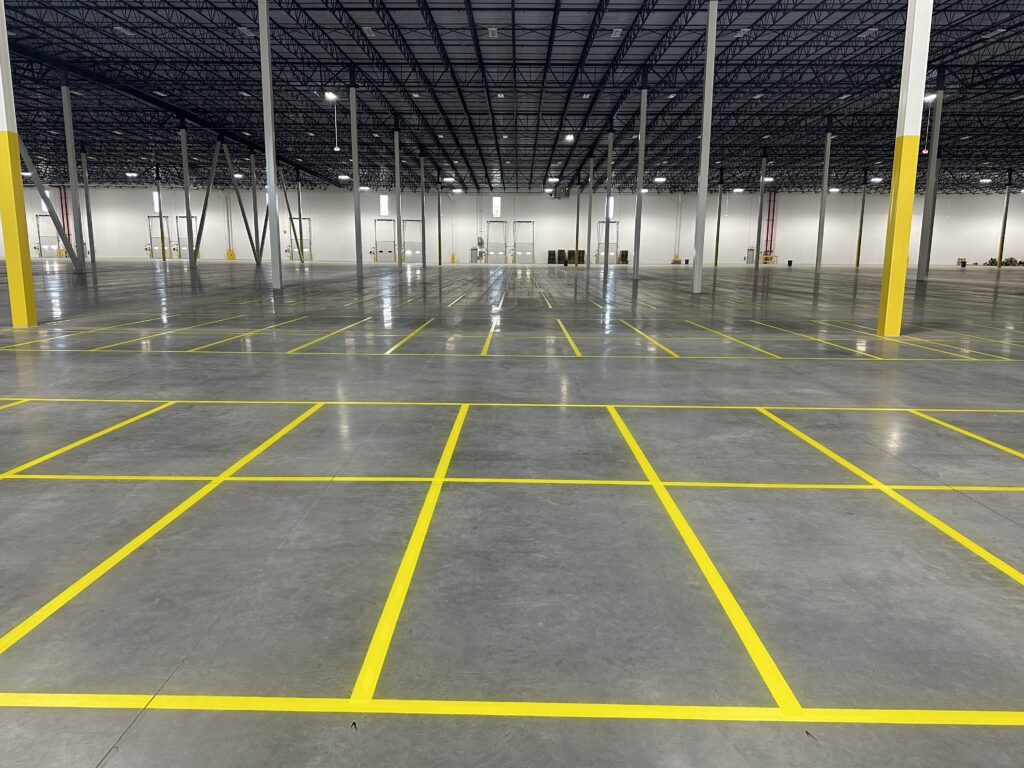 Empty warehouse interior with yellow floor markings and tall steel columns under a high ceiling, ready for storage.