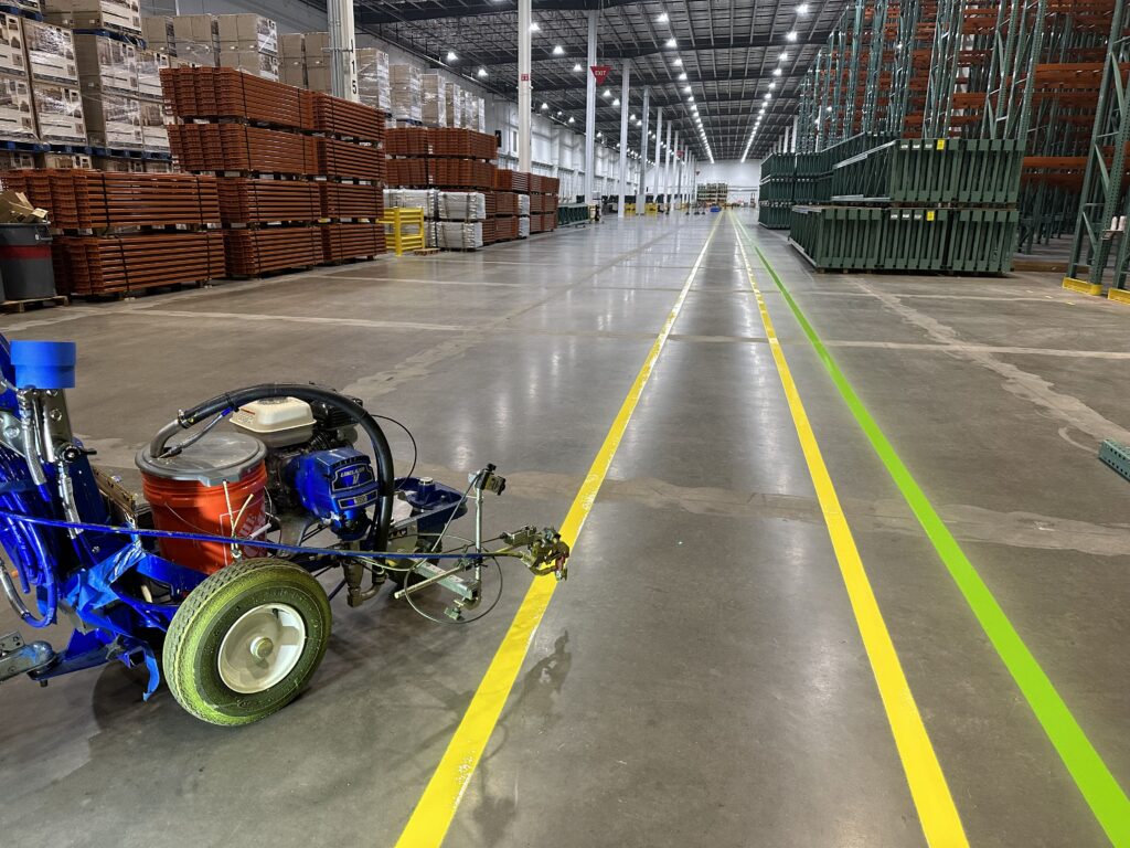 Yellow pedestrian walkway striping inside a large warehouse with loading docks and pallet racks